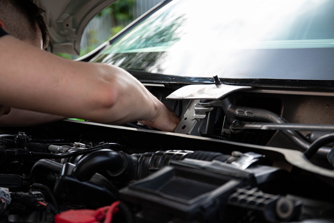 Mechanic performing engine maintenance on a car outdoors, focusing on repair work.